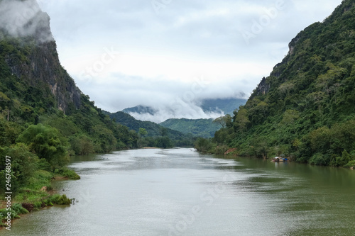 Nam Ou river view with small long boat sailing. A valley surrounded by steep limestone cliffs covered with jungle. Image taken in Nong Khiaw - a village in the Luang Prabang Province of northern Laos. © Skaniai