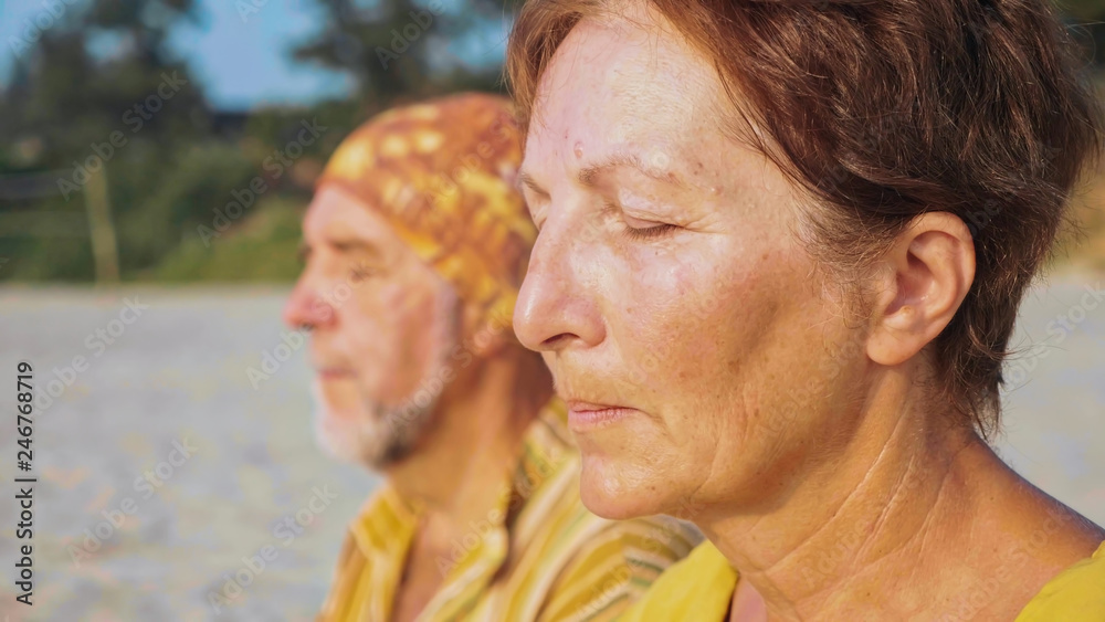 Close-up portrait of senior couple sits and meditating together on sandy beach Close-up portrait of senior couple sits and meditating together on sandy beach
