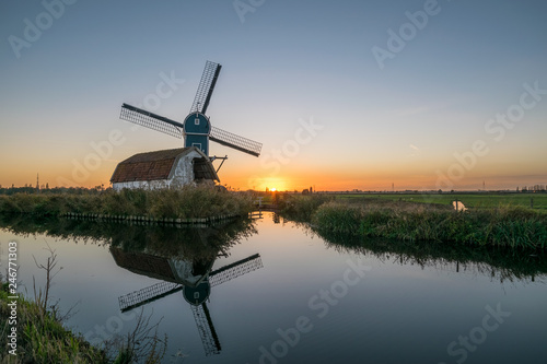 Windmill and decayed house in the dutch countryside near Leiden, Holland at sunset. The mill is beautifully reflected in the calm water of the canal.