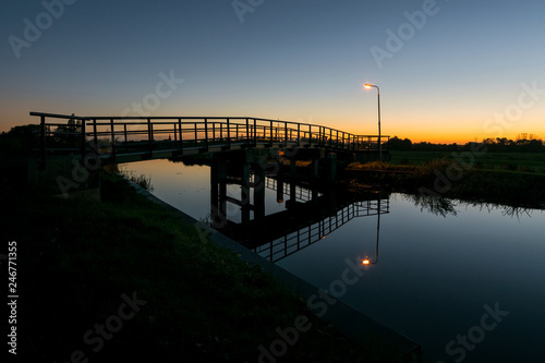 Bicycle bridge with lantern over a canal in The Netherlands after sunset.