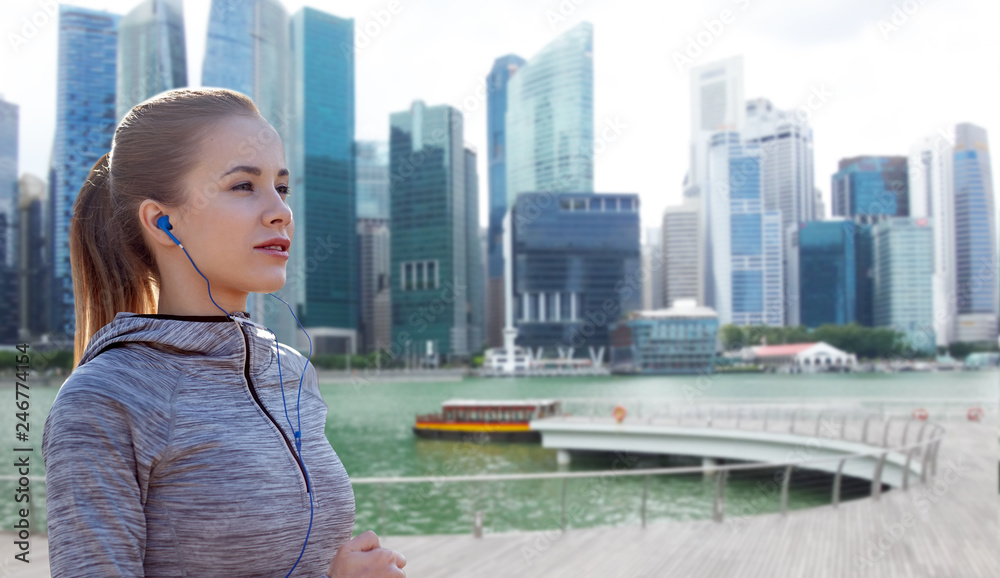 fitness, sport and people concept - happy woman running and listening to music in earphones over singapore city marina background