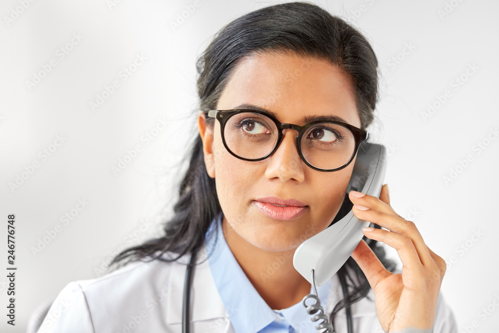 medicine, people and healthcare concept - indian female doctor in glasses calling on phone at hospital medicine, people and healthcare concept - indian female doctor in glasses calling on phone at hospital