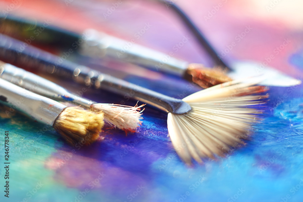 Several brushes with different bristles and palette knife lie on the palette, painted with blue, pink and purple oil Several brushes with different bristles and palette knife lie on the palette, painted with blue, pink and purple oil