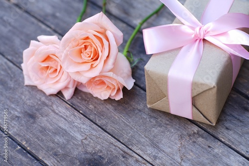 Lovely soft orange pink color rose tied by pink ribbon and brown gift box on wood table background  sweet valentine present concept