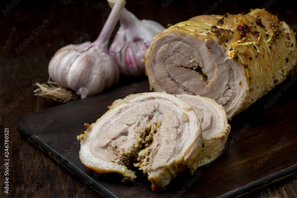 Fototapeta premium Roasted sliced pork with sauce and garnish on dark wooden old table.