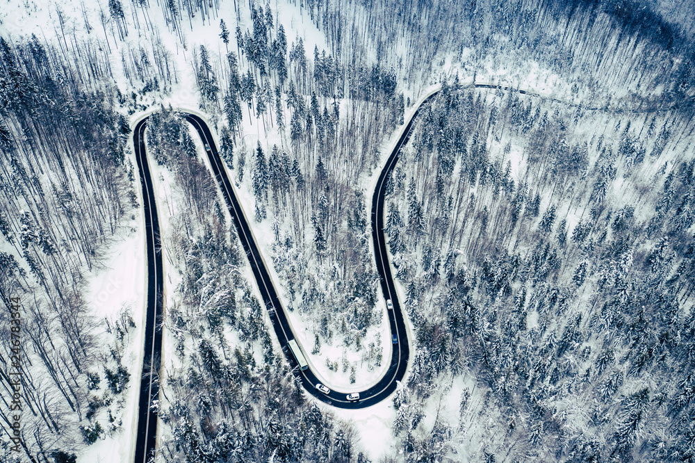 Curvy windy road in snow covered forest, top down aerial view. Winter landscape.