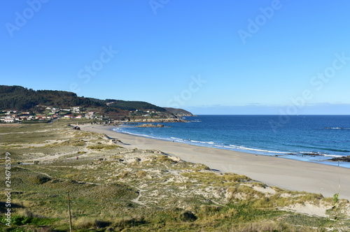 Beach and sand dunes with morning light. Rocks and blue sea with small waves and foam. Sunny day, clear sky. Galicia, Spain. © JB