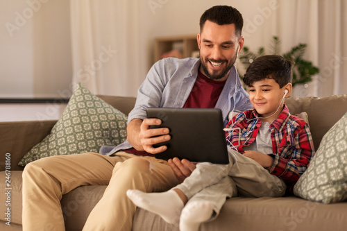 family, fatherhood and technology concept - happy father and little son with tablet pc computer and earphones listening to music at home