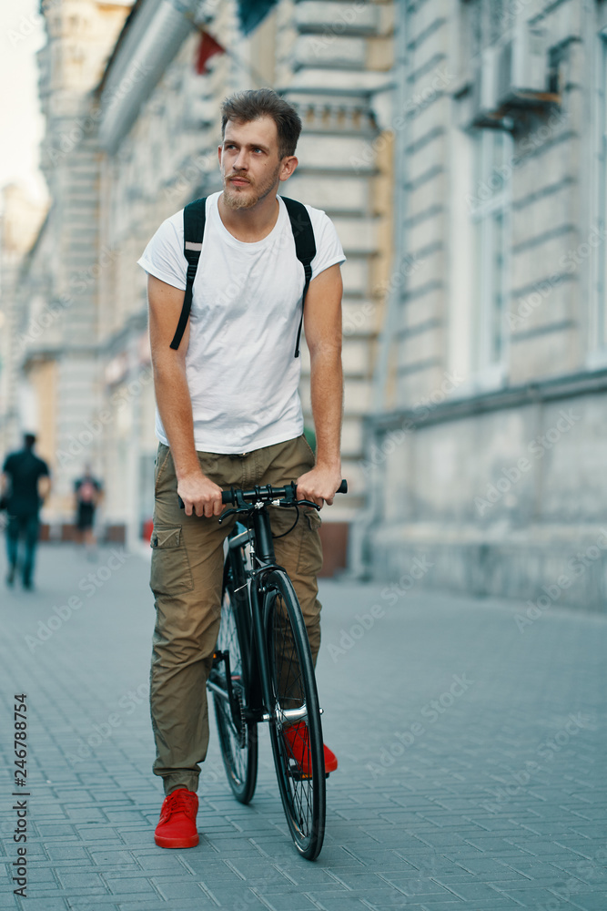 Portrait of young man walking with thoughtfully classic bicycle on city streets