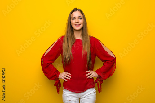 Young girl with red dress over yellow wall posing with arms at hip and laughing looking to the front