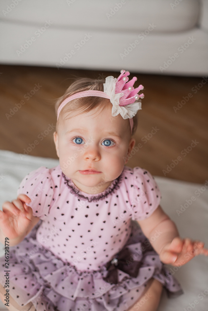 Little cute blue-eyed girl in a pink dress with a crown on her head. Portrait of the baby at home. Happiness. Cozy. Birthday. Little cute blue-eyed girl in a pink dress with a crown on her head. Portrait of the baby at home. Happiness. Cozy. Birthday.