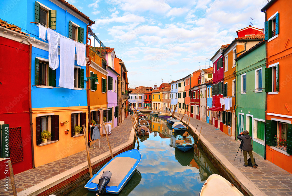  Burano island picturesque street with small colored houses in row, windows, doors and water canal with fisherman boat. Venice Italy