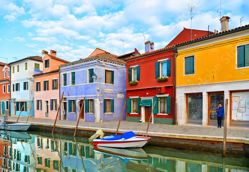  Burano island picturesque street with small colored houses in row, windows, doors and water canal with fisherman boat. Venice Italy