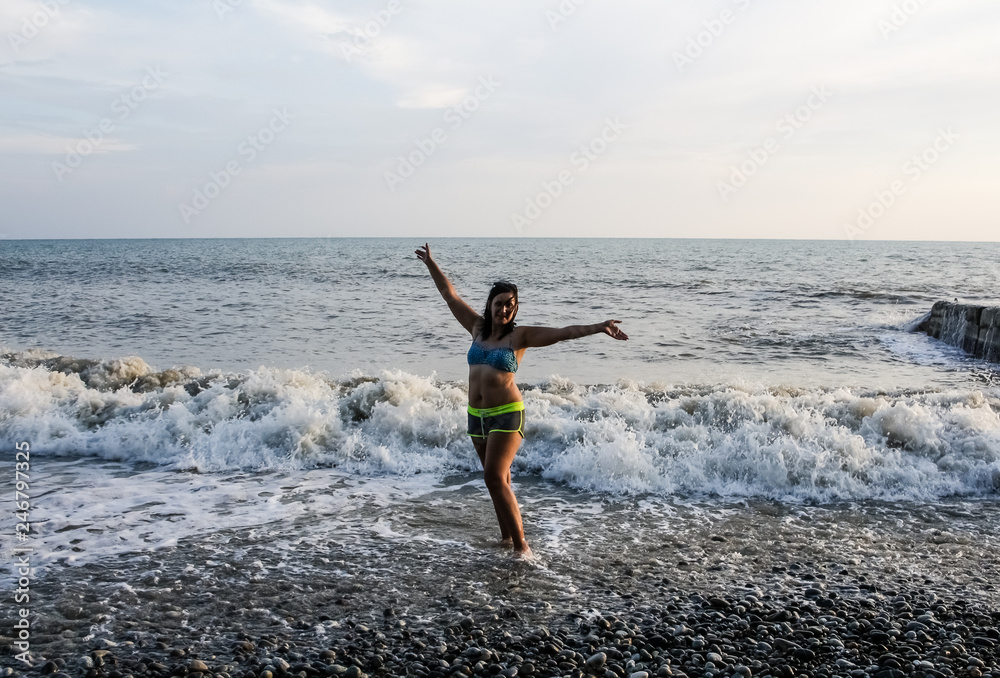 A girl is dancing on the seashore, her feet are washed by sea foam and waves.