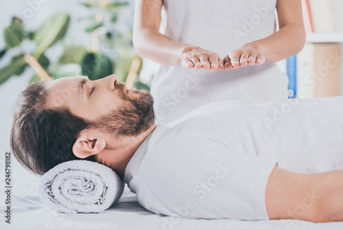 cropped shot of calm bearded man with closed eyes receiving reiki treatment on chest