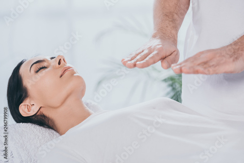 cropped shot of young woman with closed eyes receiving reiki healing session