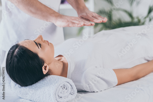 young woman lying on massage table and receiving reiki treatment