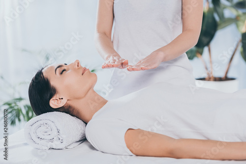 cropped shot of peaceful young woman with closed eyes receiving reiki healing treatment