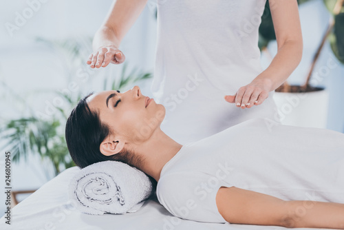 cropped shot of calm young woman receiving reiki healing therapy on head and chest