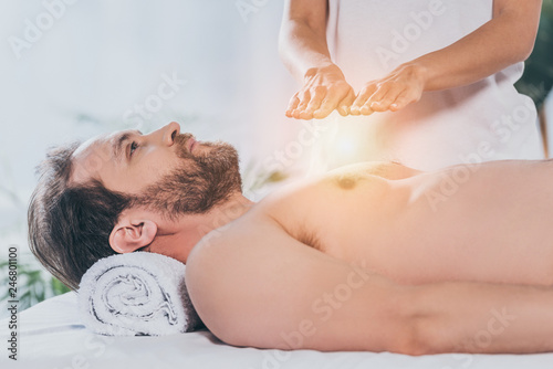 side view of bearded man looking up while receiving reiki treatment on bare chest