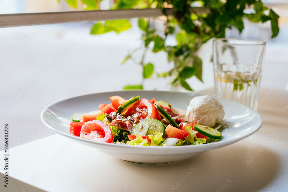 Plate of salad with tomatoes, cucumber, bell pepper, cream cheese, ham on the white table. Glass of iced water with mint and lemon. Plate of salad with tomatoes, cucumber, bell pepper, cream cheese, ham on the white table. Glass of iced water with mint and lemon.