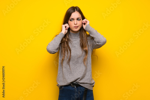 Young woman over yellow wall covering ears with hands. Frustrated expression