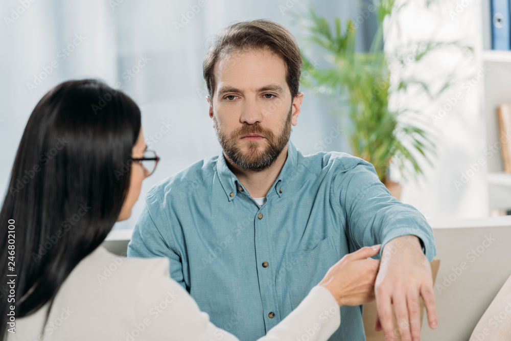 Fototapeta premium young woman in eyeglasses holding hand of bearded man during hypnotherapy