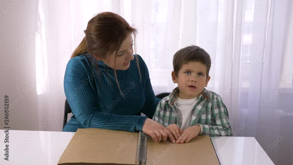 difficult schooling for blind children, young teacher teaches Visually impaired boy to read braille books with symbols font sitting at table in bright room difficult schooling for blind children, young teacher teaches Visually impaired boy to read braille books with symbols font sitting at table in bright room