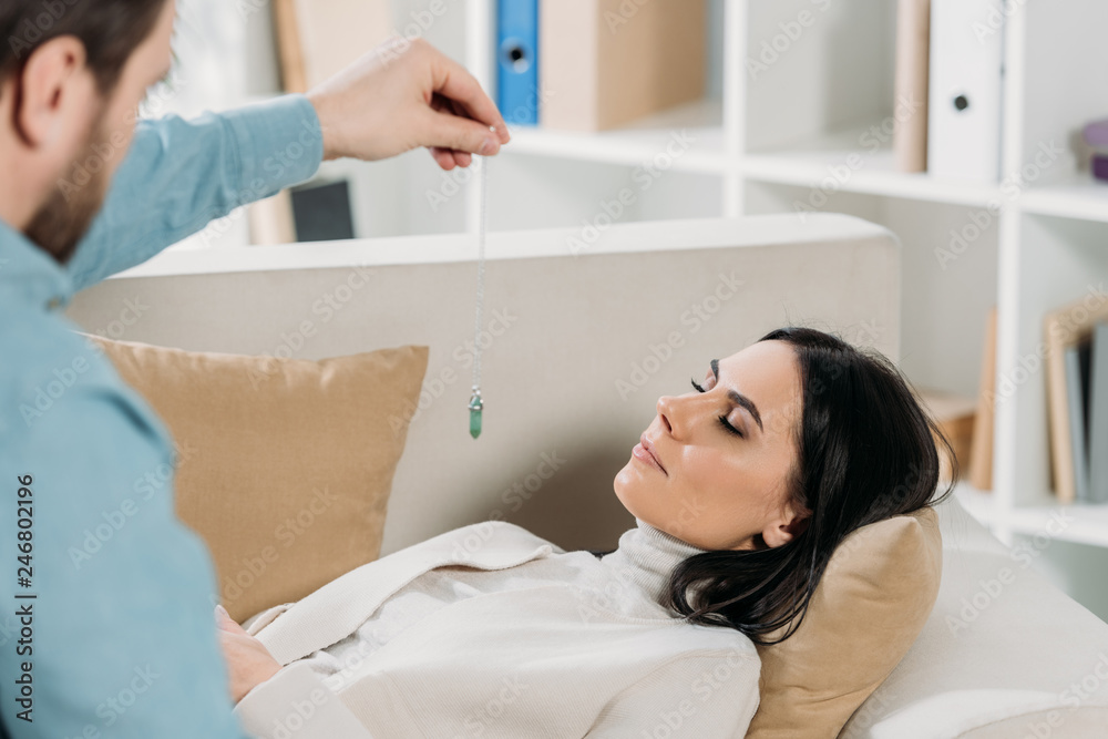 cropped shot of bearded hypnotist hypnotising young woman with closed eyes lying on couch