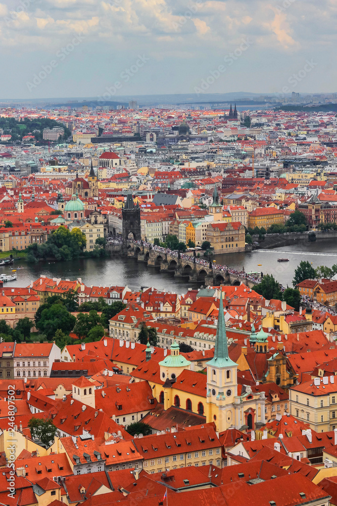 Obraz premium The panoramic view of Prague from the observation desk of Cathedral churh of St. Vitus, Czech Republic. Red roofs, churches, the Charles Bridge and the Vltava river. Cloudy rainy day.