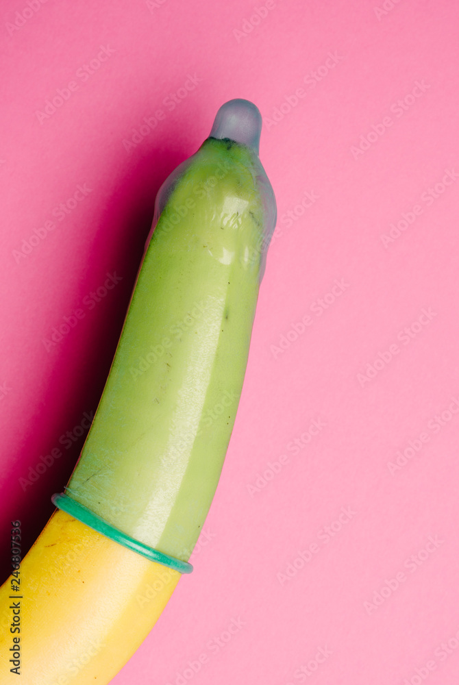Fototapeta premium Close up of green condom on fresh yellow banana in front of pink background