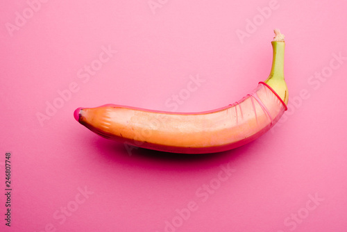 Pink condom on fresh banana in front of pink background
