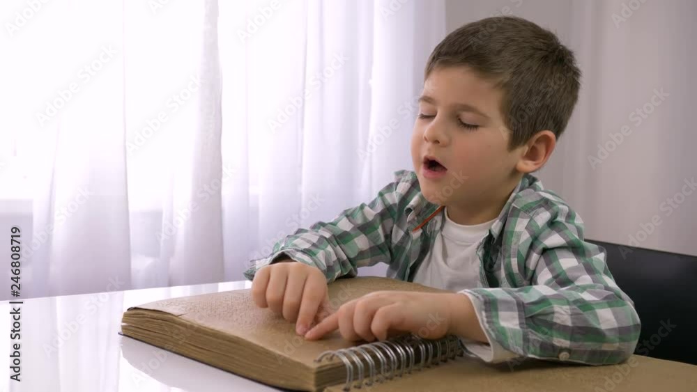 learning for blind, ill kid boy reading braille book with characters font for Visually impaired sitting at table indoors learning for blind, ill kid boy reading braille book with characters font for Visually impaired sitting at table indoors