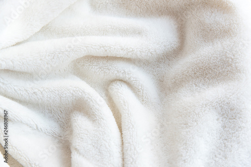 White delicate soft  background of plush fabric. Texture of beige soft fleecy blanket textile with twisted folds.