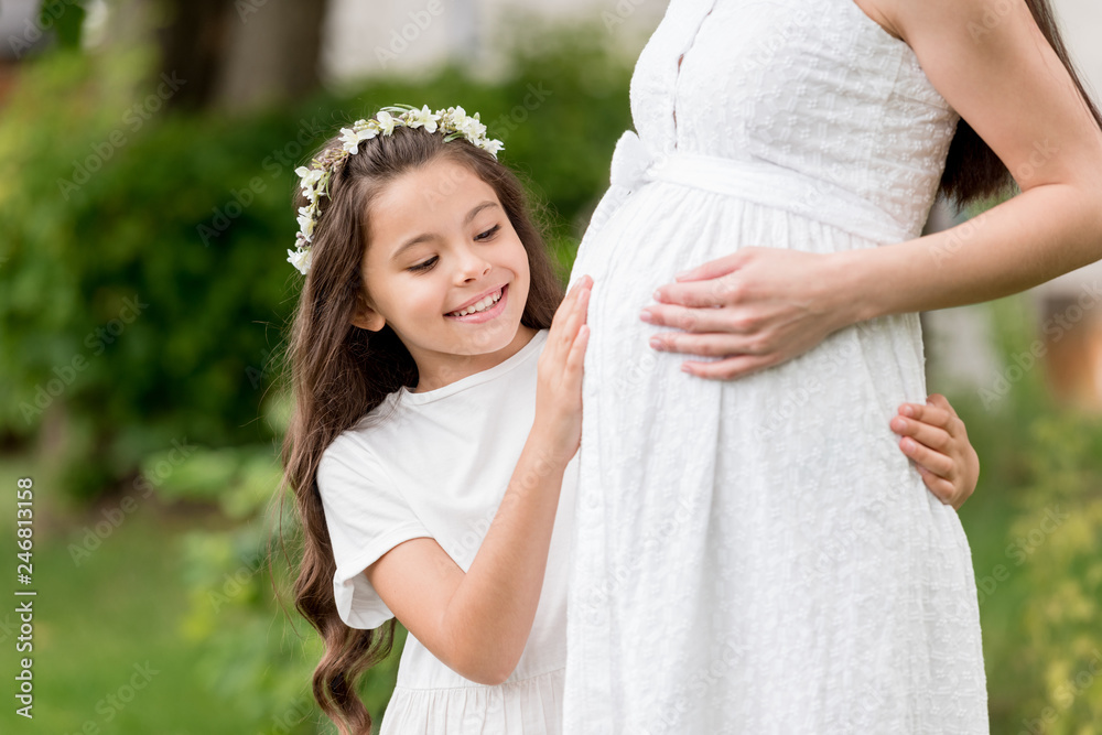 cropped shot of adorable happy child in floral wreath touching belly of pregnant mother in park cropped shot of adorable happy child in floral wreath touching belly of pregnant mother in park