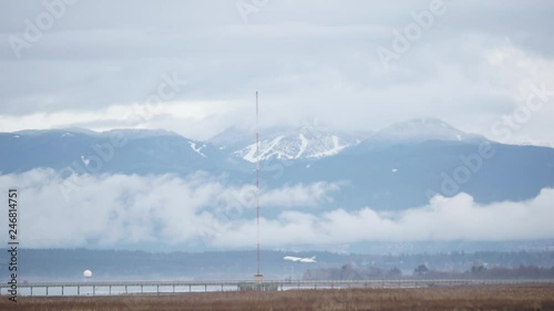 Plane flying over the Dike in Vancouver, BC. Mountain landscape behind with cloud cover. Shot on the Sony 50-210mm on a Sony A5100. photo