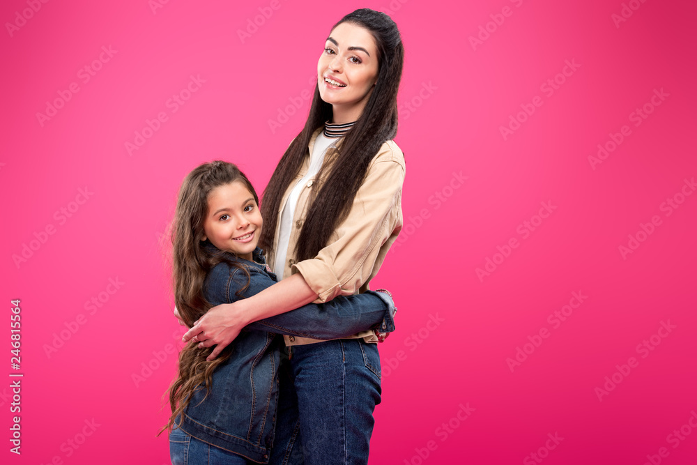 side view of beautiful happy mother and daughter hugging and smiling at camera isolated on pink side view of beautiful happy mother and daughter hugging and smiling at camera isolated on pink