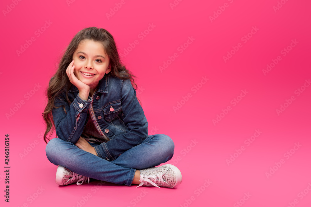 adorable happy child in denim clothes sitting with hand on chin and smiling at camera on pink adorable happy child in denim clothes sitting with hand on chin and smiling at camera on pink