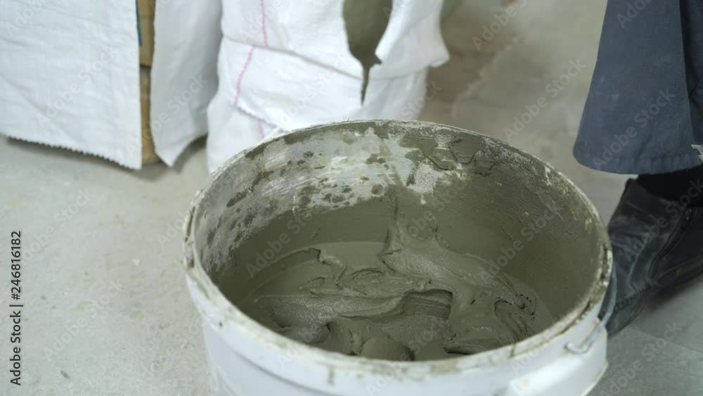 closeup of construction worker taking adhesive solution from bucket with trowel closeup of construction worker taking adhesive solution from bucket with trowel