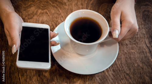 girl sits in a cafe and holds a cup of tea and a phone in her hands, waiting for a call