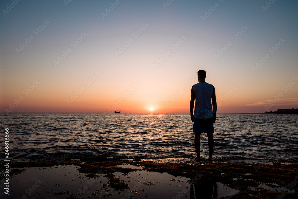 man looks at the sunset at the sea