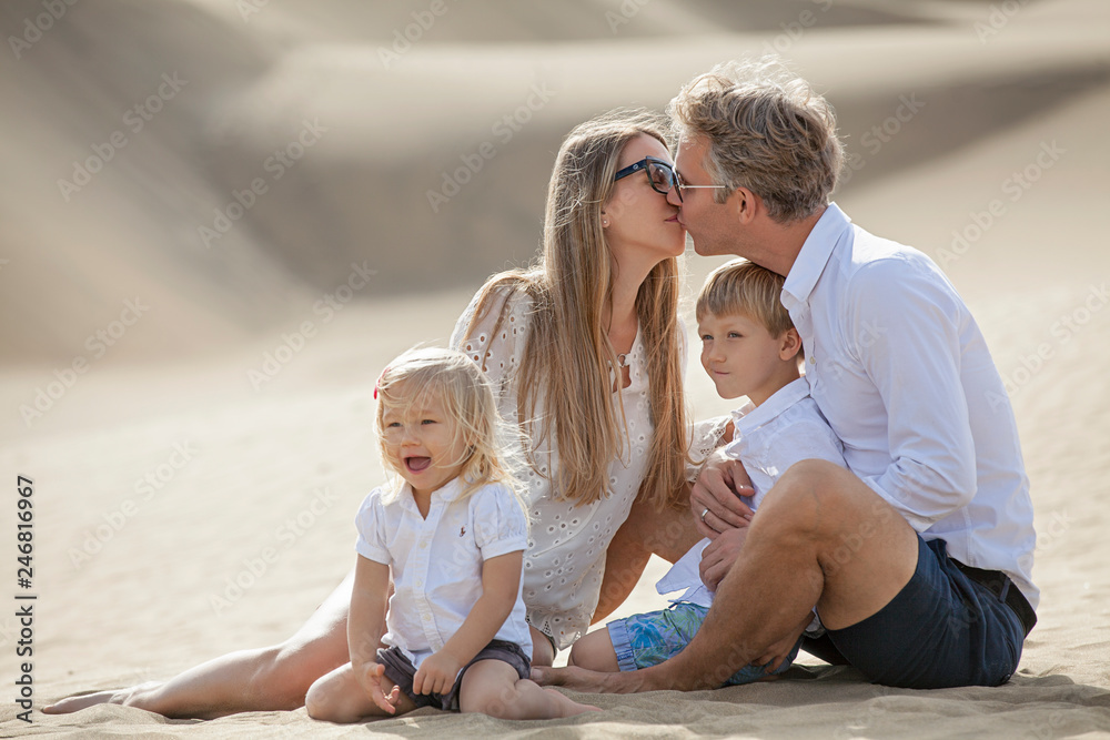 happy family in white shirts sits on the sand. Mom kisses dad happy family in white shirts sits on the sand. Mom kisses dad