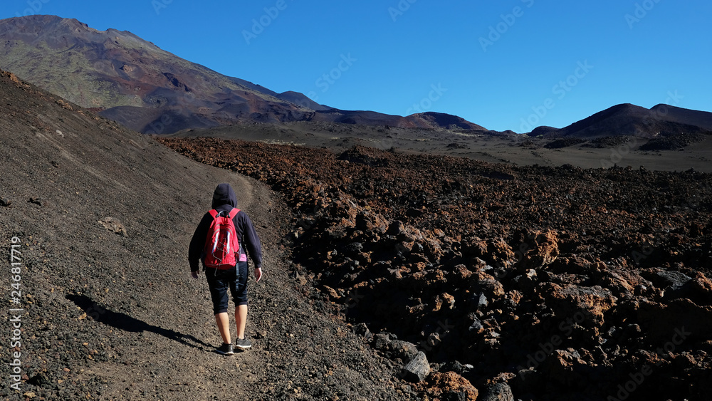 Female hiker walking the path through the volcanic landscape of Montaña Samara, towards Pico Viejo and Las Cuevas Negras with Aa lava on the right, at Montana Samara, Teide National Park, in Tenerife Female hiker walking the path through the volcanic landscape of Montaña Samara, towards Pico Viejo and Las Cuevas Negras with Aa lava on the right, at Montana Samara, Teide National Park, in Tenerife