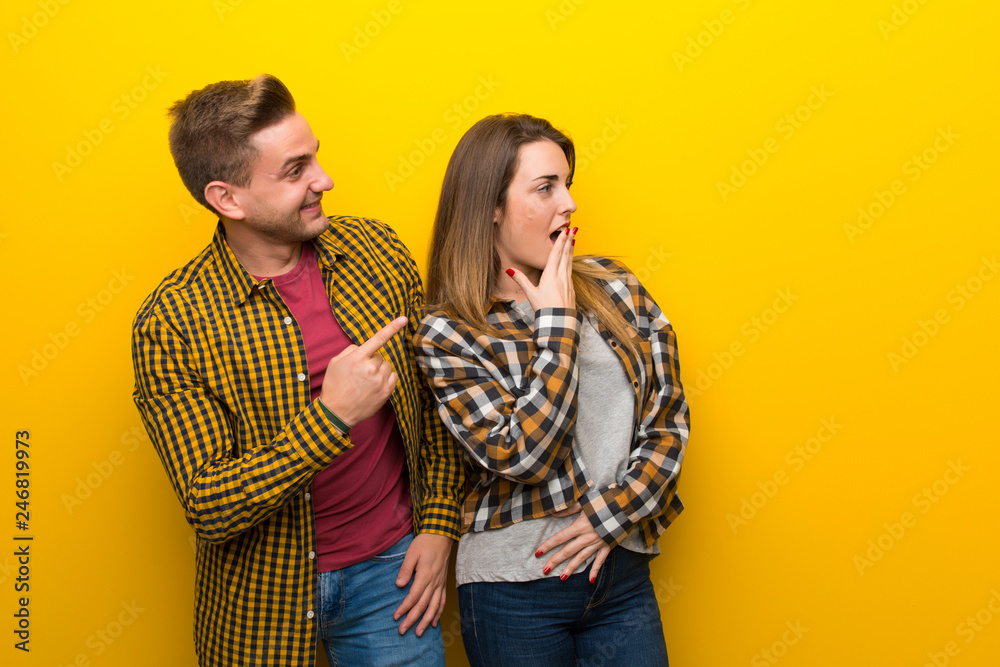 Couple in valentine day pointing finger to the side with a surprised face Couple in valentine day pointing finger to the side with a surprised face