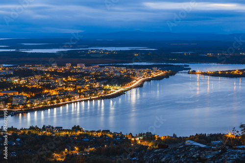 Panoramic view from the summit on the living district of northern city Monchegorsk with night lighting surrounded by taiga forest, mountains, and many lakes. Kola peninsula, Murmansk region, Russia