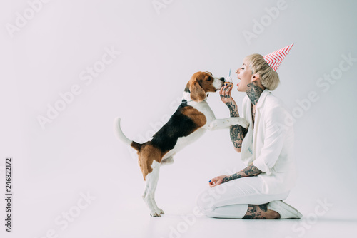 happy blonde woman eating cupcake while sitting near beagle dog on grey background