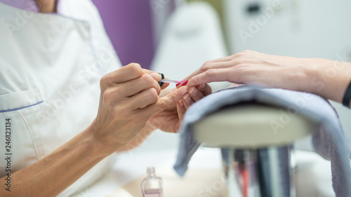 Closeup of manicurist applying shiny pink nail polish