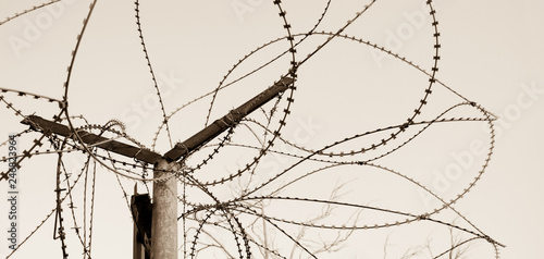 Rusty barbed wire and sky at background. War  illegal migration  imprisonment concepts. Sepia photo.