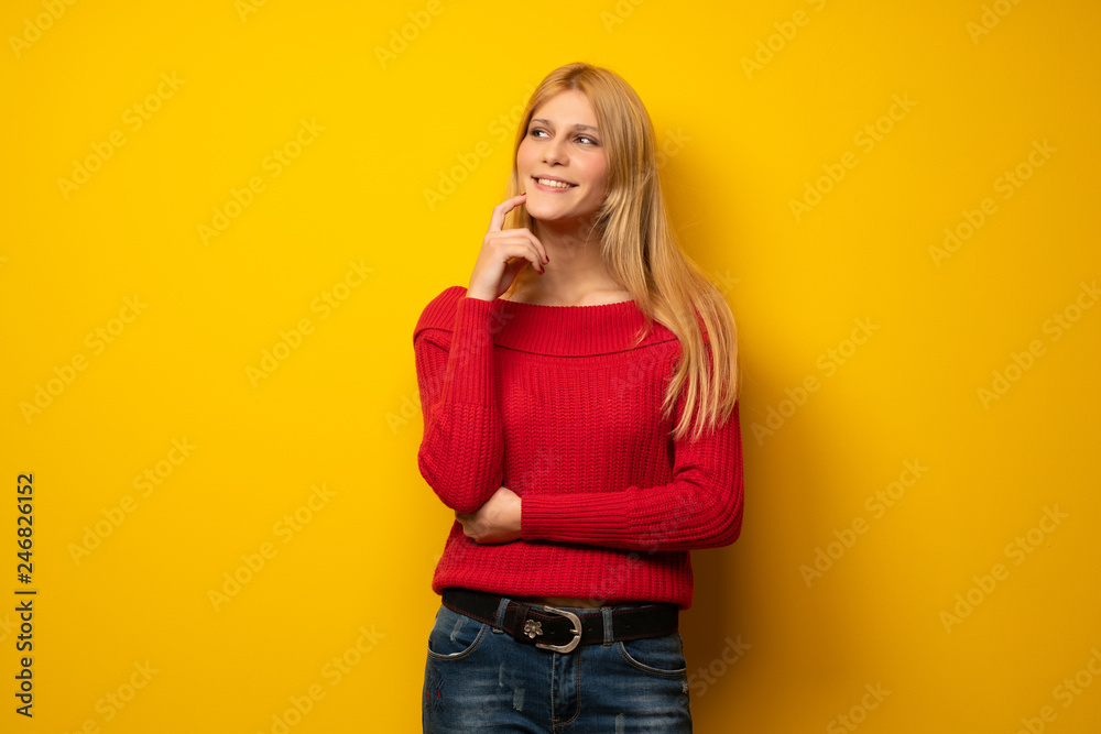 Blonde woman over yellow wall thinking an idea while looking up