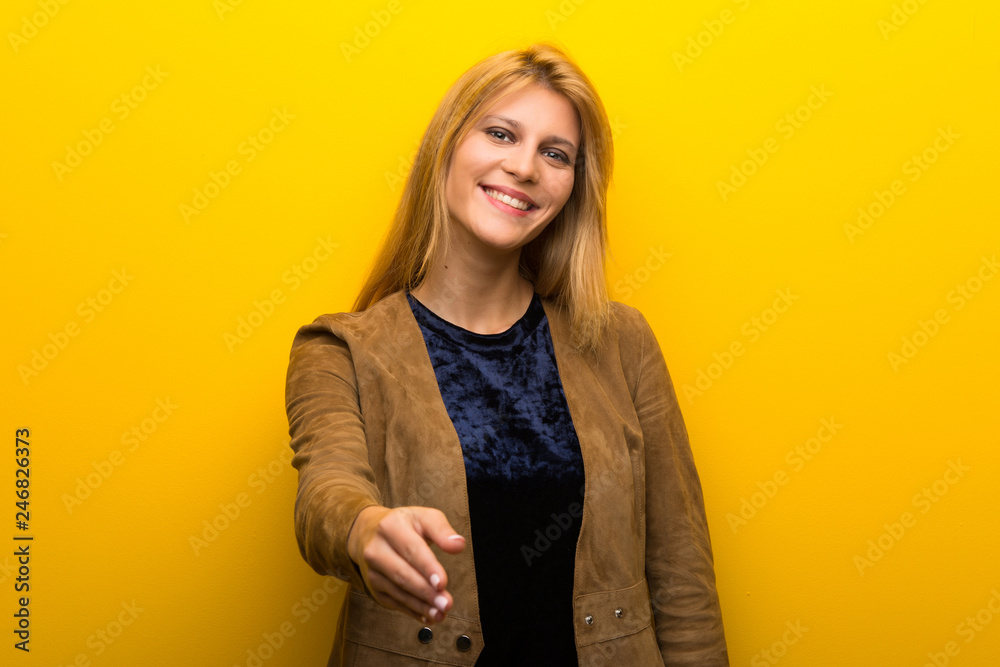 Blonde girl on vibrant yellow background shaking hands for closing a good deal Blonde girl on vibrant yellow background shaking hands for closing a good deal